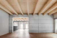 Large empty room with timber beams, an oak floor and a concrete wall opening onto the lattice windows