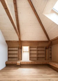 Attic room under old roof rafters with built in shelving, a bench and a small gable window