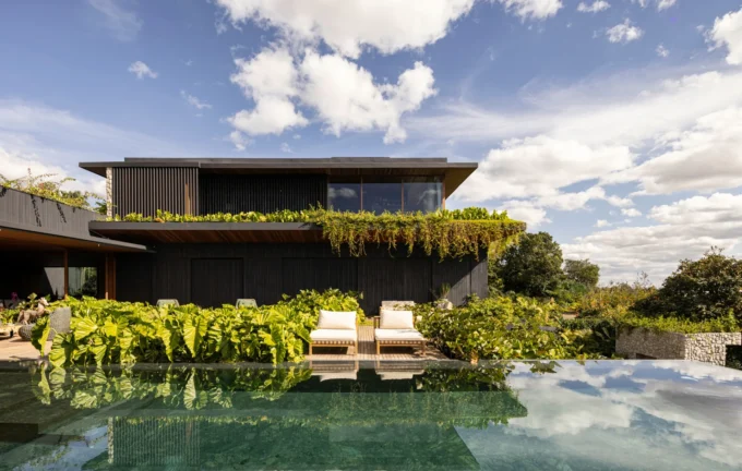 Dark two storey house draped in plants behind an infinity pool and sun loungers, Vista House by Studio Gontijo Arquitetura