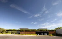 Low street front with a long timber clad base, garage and a planted roof edge under a wide sky, Vista House by Studio Gontijo Arquitetura