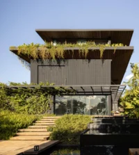 Black upper volume with a deep overhang and hanging plants above a glazed gym and stepping stones, Vista House by Studio Gontijo Arquitetura