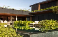 Covered terrace with outdoor sofas behind a dark green pool edged with dense tropical planting, Vista House by Studio Gontijo Arquitetura