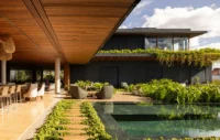 Timber soffit over an outdoor dining area beside a pool, with stepping stones set in lawn strips, Vista House by Studio Gontijo Arquitetura