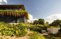Planted roof edge of the upper floor above a lush garden and a stone retaining wall, Vista House by Studio Gontijo Arquitetura