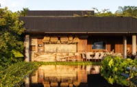 Lounge pavilion with a stone fireplace wall and timber ceiling reflected in a black pool, Vista House by Studio Gontijo Arquitetura