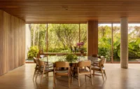 Dining table with wooden chairs in a timber lined room opening fully to the garden, Vista House by Studio Gontijo Arquitetura
