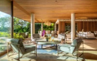 Open living area with armchairs and a round table under a wood ceiling between concrete columns, Vista House by Studio Gontijo Arquitetura