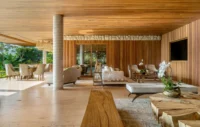 Long living space with travertine floor, wood panelled walls and several seating groups, Vista House by Studio Gontijo Arquitetura